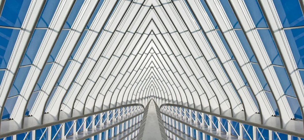 Modern glass tunnel with white triangular beams and central walkway.
