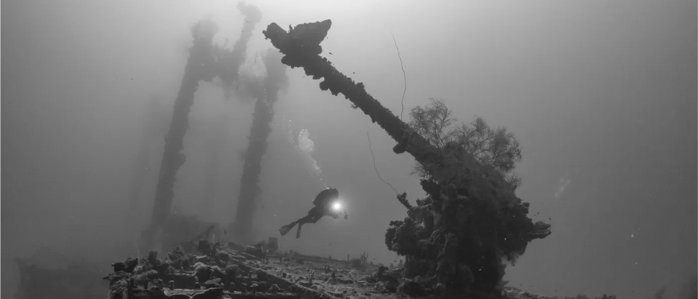 A scuba diver is underwater near the wreck of a ship.