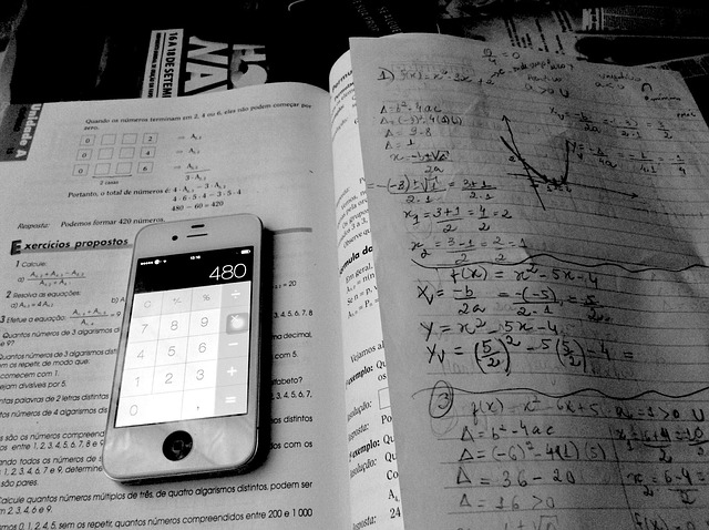 Open math textbook with a phone calculator displaying '480' and a notebook with algebra equations.