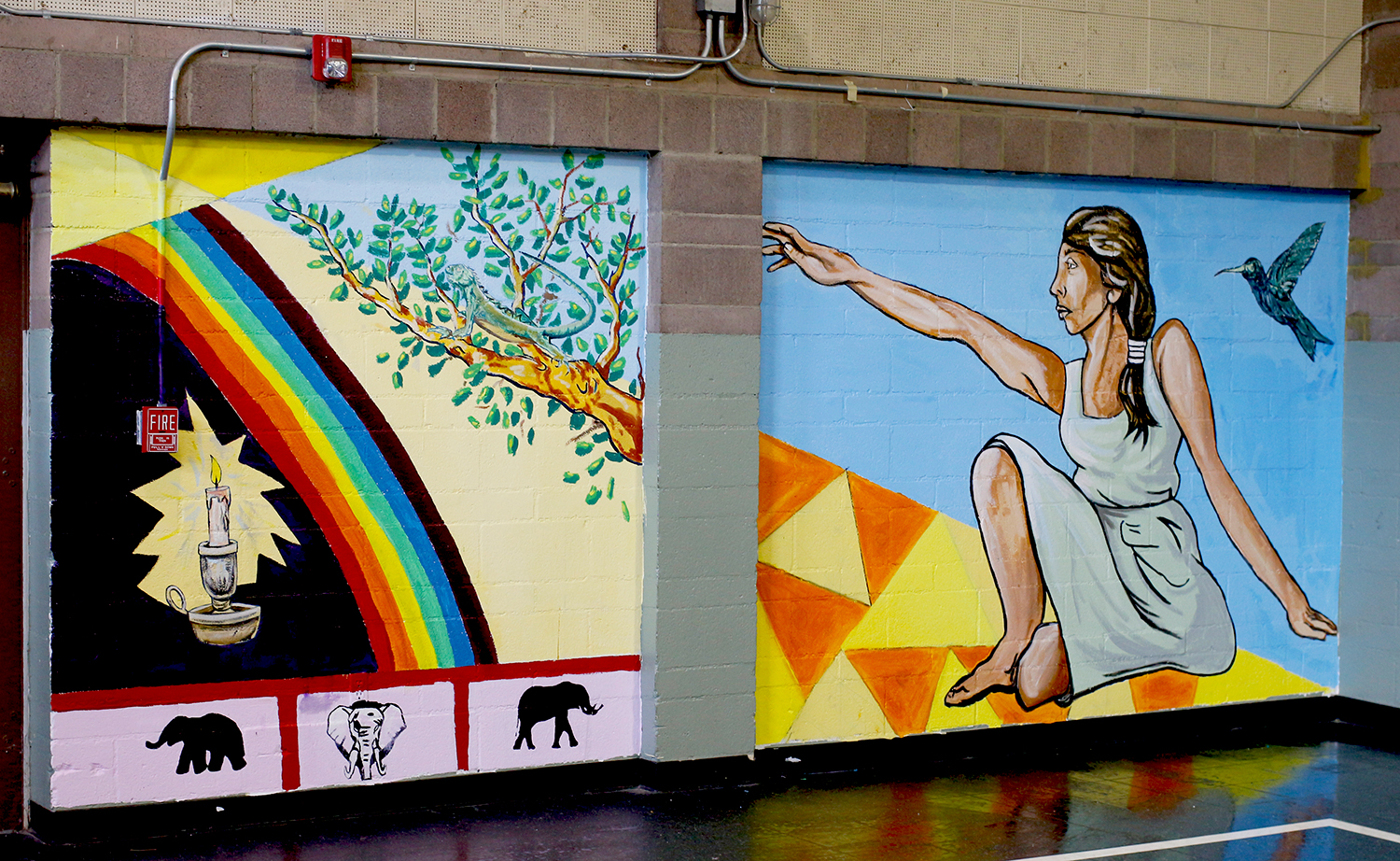Mural with rainbow, candle, woman, and other imagery in juvenile detention camp basketball court. 