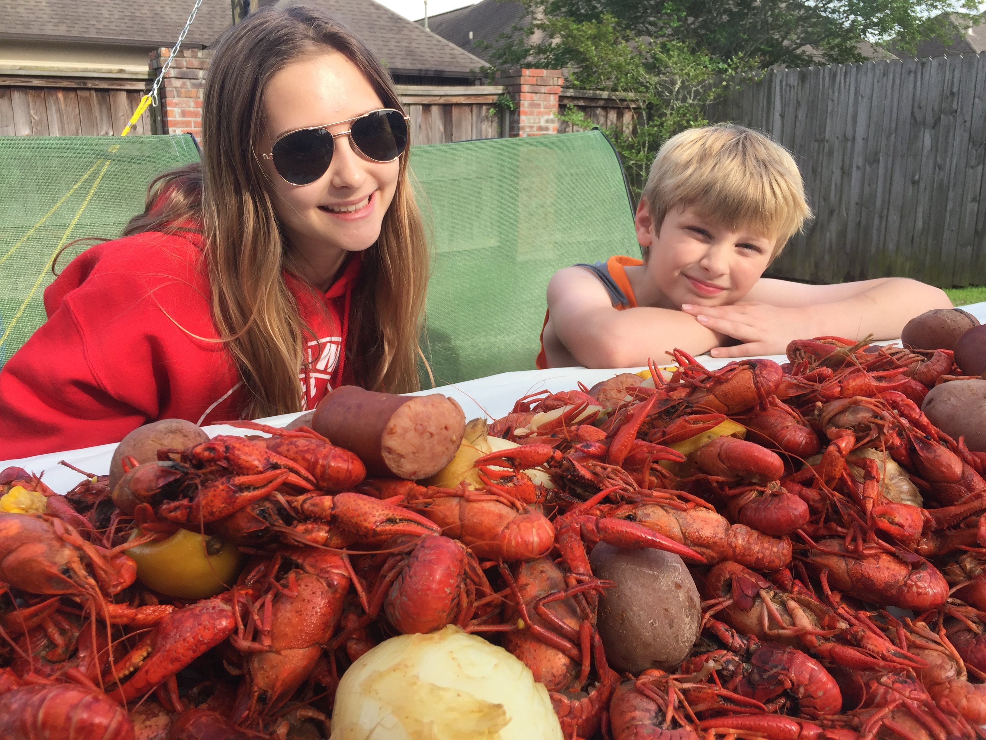 This image shows a meal of boiled crawfish with corn and potatoes and smiling children gathered around a table, enjoying fami