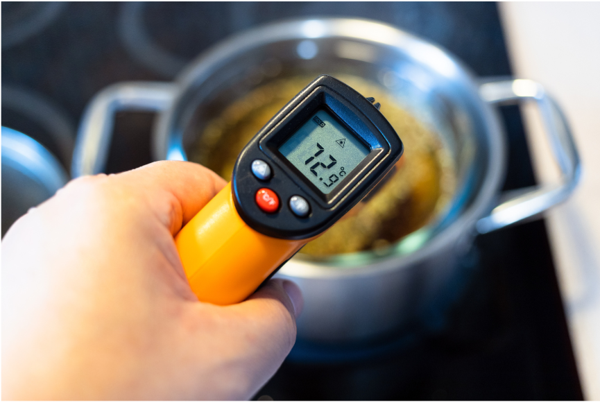 The hand of a food employee using a thermometer to measure the temperature of a pot of soup.